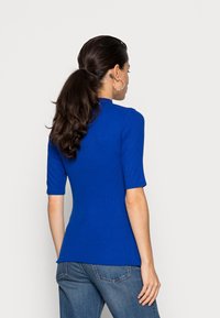 Blaues geripptes Strickoberteil mit kurzen Ärmeln, taillierte Passform und rundem Ausschnitt, kombiniert mit Jeans. Minimalistischer Stil, glatte Textur.