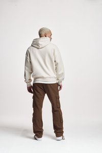 Felpa beige con un ampio cappuccio, polsini a coste, abbinata a pantaloni cargo marroni con tasche laterali. Modello di spalle, su uno sfondo neutro.