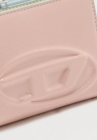 Κοντινό πλάνο ενός ροζ δερμάτινου αντικειμένου με ανάγλυφο οβάλ λογότυπο που φέρει τα γράμματα "LD" σε ραμμένη επιφάνεια.