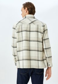 Heren flanellen overhemd in crème met een zwart en bruin ruitpatroon, voorzien van een puntkraag, lange mouwen en knoopsluitingen aan de manchetten.