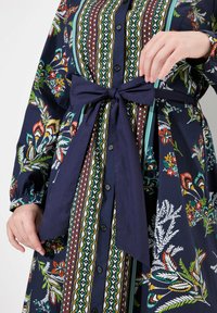 Robe chemise à motifs floraux en bleu marine, ornée d'imprimés botaniques colorés, avec un devant à boutons et une ceinture en tissu nouée à la taille.