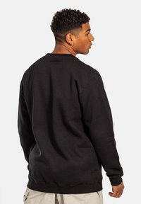 Sudadera negra con cuello redondo y puños acanalados, que presenta una textura suave y un diseño minimalista, vista desde la parte posterior.