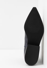 Décolleté con tomaia testurizzata di un blu scuro, punta affilata e suola in gomma nera con scanalature per una presa migliore. Taglia 37.