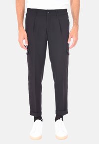 Pantaloni cargo neri con vestibilità rilassata, design plissettato, tasche laterali e orli a sbuffo, abbinati a sneaker bianche su uno sfondo neutro.