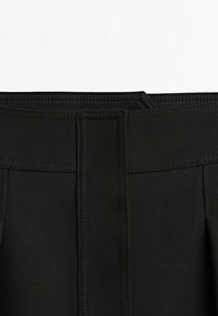 Pantalon noir taille haute avec devant plat, présentant des détails de couture subtils, une texture lisse et des poches latérales dans une coupe ajustée.