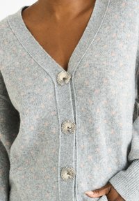 Gray knitted cardigan with pink polka dots, V-neckline, three metallic floral buttons, and ribbed cuffs. Soft texture and relaxed fit.