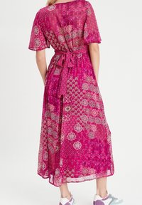 Lyserød, mønstrede maxi-kjole med korte ærmer, bånd i taljen og letvægtsstof; har blomster- og geometriske designs. Sneakers synlige.