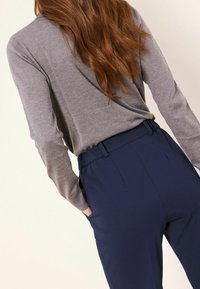 Šedé tričko s dlouhým rukávem s volným střihem spojené s tmavě modrými kalhotami s vysokým pasem, které mají pás a boční kapsy.