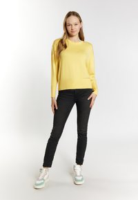 Keltainen neulepusero, jossa on pyöreä pääntie, yhdistettynä mustiin slim fit -farkkuihin ja monivärisiin korkeavartisiin tennareihin. Sujuva pinta, rento muotoilu.