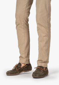 Dunkelgrüne Wildleder-Lederslipper mit braunen Schnürsenkeln und Nähten; kombiniert mit beigefarbenen, taillierten Hosen. Glatte Textur und Slip-on-Design.
