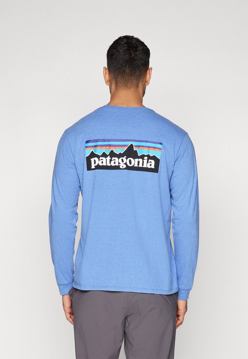 Hosszú ujjú, puha anyagból készült kék ing, amelyen egy sokszínű hegyi grafika látható "Patagonia" felirattal, fekete háttérrel.
