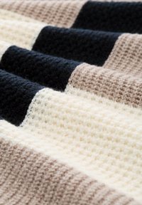 Couverture tissée présentant des rayures alternées de crème, beige et noir, avec une surface texturée et un design en tricot épaissi.