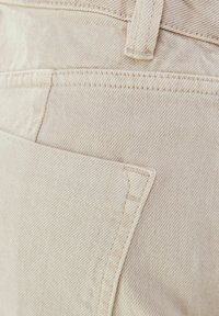 Beige denim fabric with a textured surface, featuring a large front pocket and contrasting stitching along the edges.