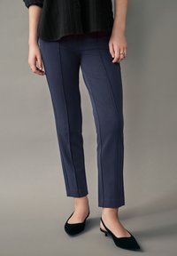 Pantalones azul marino de corte ajustado, con costuras verticales. Combinados con tacones de slingback negros en suave terciopelo, que se estrechan en la punta.