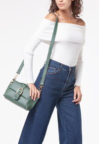 Borsa a tracolla verde in pelle con chiusura a patta, accessori in oro e tracolla regolabile. Presenta una forma rettangolare e una superficie texturizzata.