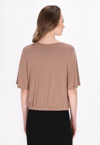 Bruine, korte mouwen, cropped top van zacht materiaal; heeft een ronde halslijn en een elastische tailleband, gecombineerd met een zwarte rok.