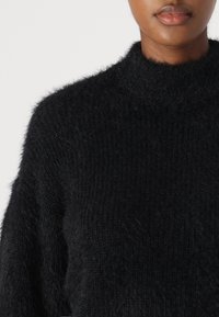 Maglione nero con un collo alto, realizzato in un materiale morbido e soffice; presenta una vestibilità ampia e una superficie testurizzata.