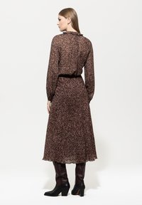Langärmliges, knielanges Kleid in einem braunen Leopardenmuster, aus leichtem Stoff, mit einem Rüschenausschnitt und elastischem Bund. Schwarze Absatzstiefel.
