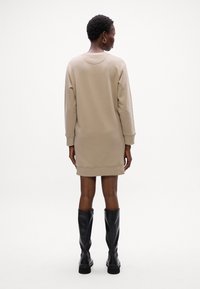 Beige Sweatkleid mit langen Ärmeln, gerippten Bündchen und Saum, mit Rundhalsausschnitt und bequemer Passform, kombiniert mit schwarzen kniehohen Stiefeln.