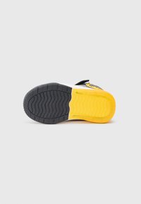 Sole di sneaker nera e gialla con schemi di presa texturizzati, divisa tra sezioni grigie scure e gialle brillanti, caratterizzata da un design distintivo.