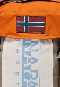Sac en tissu orange avec un patch marron arborant une croix bleue. Panneau blanc en dessous avec du texte bleu. Design robuste avec des coutures visibles.