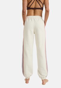 Lichtbeige joggingbroek met elastische boorden, voorzien van zijstrepen in lila en oranje. Zachte stof met een relaxte pasvorm en een elastische tailleband.