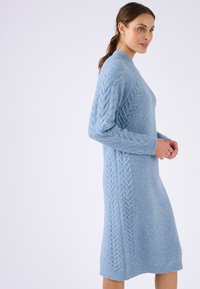 Abito lavorato a maglia blu chiaro realizzato in materiale morbido, con dettagli a treccia lungo le maniche e i lati, dal taglio rilassato e lungo fino al ginocchio.