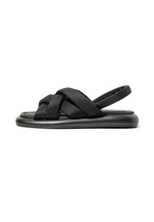 Black sandals with crossed fabric straps, open back, flat sole, and cushioned footbed. Features a minimalist design and smooth texture.