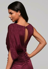 Robe bourgogne avec des épaules drapées, un dos nu et des détails en zip. Présente une texture froncée sur les côtés pour une silhouette ajustée.