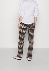 Bílá košile s texturovanými nabíranými rukávy, v kombinaci s černobílými kostkovanými kalhotami a bílými sandály, pohled zezadu.