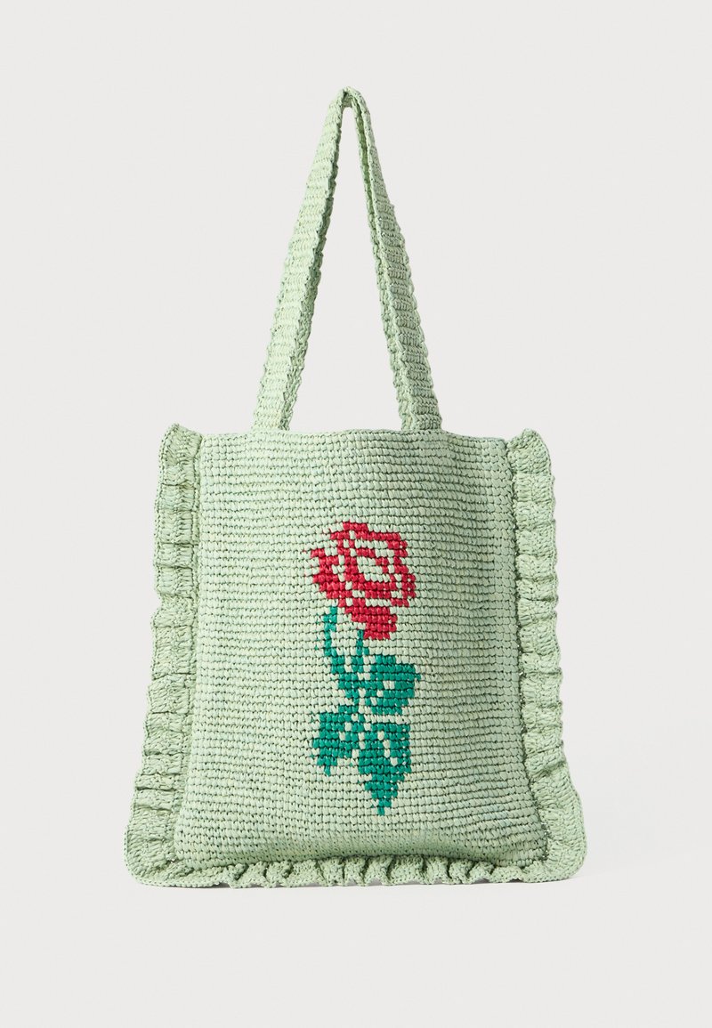 Knit tote bag in light green with a red rose and green leaves embroidered on one side. Features a ruffled edge and two textured handles.