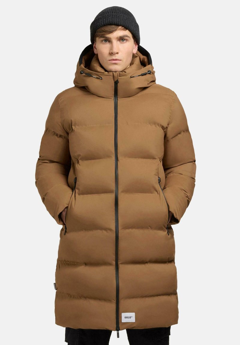 Brun polstret frakke med høj krave, lynlås og sidelommer. Har horisontalt quiltet design og mærkepatch ved kanten.