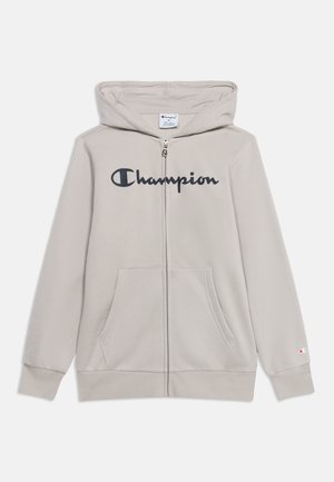 Svijetlo bež dukserica na patent s prednjim džepovima i crnim logotipom "Champion" preko prsa, s kapuljačom i dugim rukavima.