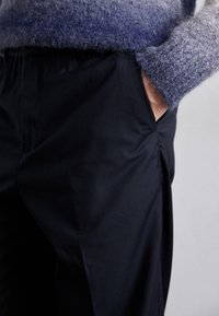 Pull en laine dégradé de tons bleus et gris, accompagné de pantalons noirs lisses avec poches latérales et détails de plis.