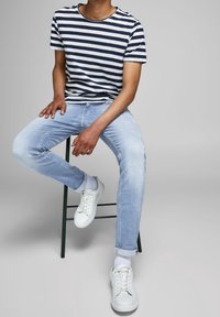 Marinblå och vit randig t-shirt, ljusblå jeans, vita sneakers. Avslappnad outfit med en lös passform och uppvikta byxben på jeansen.