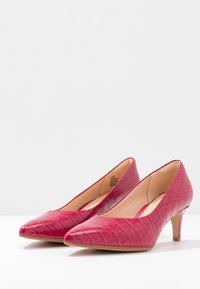 Escarpins en cuir verni rouge avec une texture crocodile, bout pointu et talon modeste. L'intérieur présente une doublure lisse et un design incurvé.
