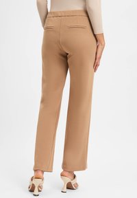 Beige polyestermix broek met een ontspannen pasvorm, elastische tailleband en twee achterzakken. Soepele textuur en recht model.
