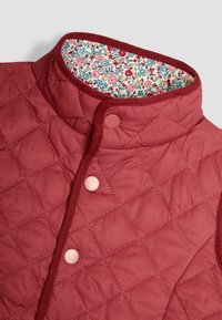 Quiltani bordo prsluk s okruglim ovratnikom i dva okrugla dugmeta. Unutrašnjost obložena tkaninom s cvjetnim uzorkom u pastelnim bojama.