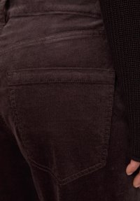 Bruine corduroy broek met een gestructureerd oppervlak en details van een achterzak. De stof toont ribbelige lijnen voor extra visuele dynamiek.