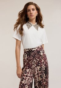 Top blanco de manga corta con cuello decorativo de cuentas, combinado con pantalones anchos de estampado floral burdeos y negro.