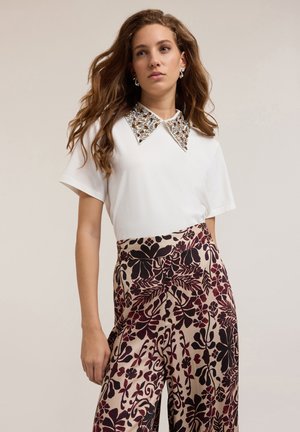 Top blanco de manga corta con cuello decorativo de cuentas, combinado con pantalones anchos de estampado floral burdeos y negro.
