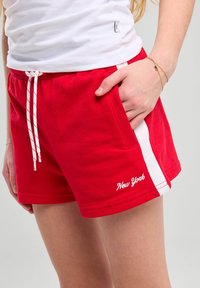 Shorts en coton rouge avec des bandes latérales blanches, dotés d'une taille élastique et d'un cordon de serrage. "New York" brodé en blanc à l'ourlet.