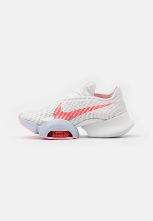 Chaussure de course Nike blanche et gris clair avec un swoosh rouge et une semelle intermédiaire incurvée distinctive dotée d’un amorti Zoom Air visible.
