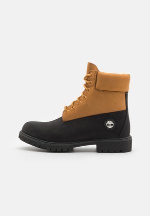 Stivaletti alla caviglia neri e marroni realizzati in pelle e suede, con un colletto imbottito, sei fori per i lacci e una suola in gomma con una toppa del logo.