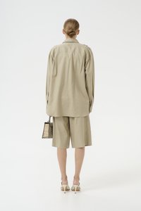 Chemise beige avec boutons sur les épaules, assortie à un short. Tissu transparent et forme structurée. Les accessoires comprennent un petit sac à motif serpent.
