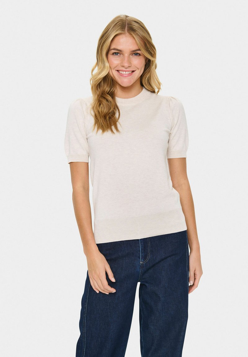Kortärmad krämfärgad tröja med rund halsringning, slät textur och en figurnära nederkant, kombinerad med mörkblå vida jeans.