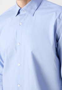 Camicia azzurro chiaro, con bottoni, dal colletto classico, realizzata in tessuto liscio, presenta una vestibilità su misura e una leggera lucentezza.