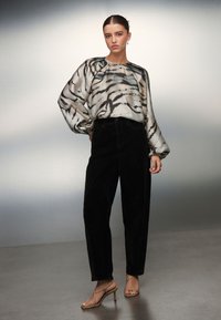 Prozirna, lagana bluza s kremastim i crnim prugastim uzorkom tigra. Hlače od crnog manšestra s visokim strukom i remenaste visoke štikle boje kože.