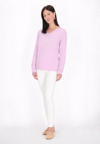 Top de culoare violet deschis, cu mânecă lungă și gât în V, asociat cu pantaloni albi, mulati, și pantofi slip-on de culoare bej. Modelul adoptă o postură relaxată.