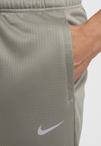 Nike urheilushortsit vaaleanharmaasta kankaasta, jossa on teksturoitu kuvio. Lyhyillä lahkeilla on sivutasku ja valkoinen logo alareunassa.
